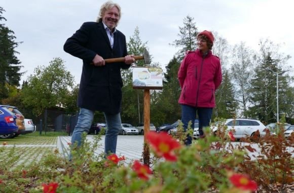 CEO Rainer Hollnagel hämmert ein Schild in den Boden des Parkplatzes. Auf dem Schild ist ein Hinweis zur Nutzung als Schmetterlings-Wiese.